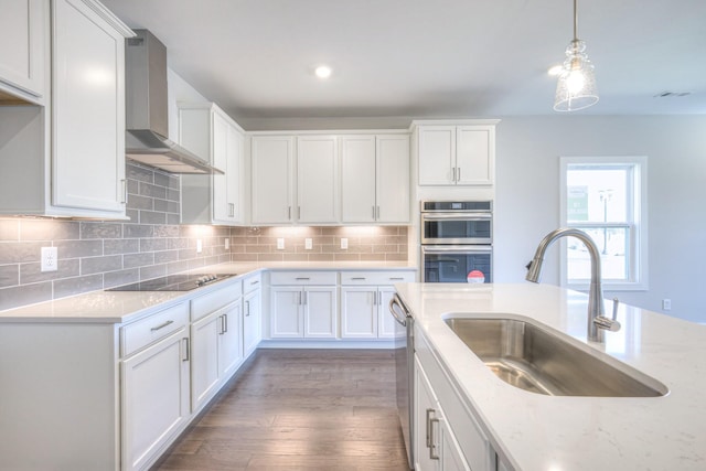 kitchen featuring stainless steel appliances, a sink, white cabinetry, wall chimney range hood, and backsplash