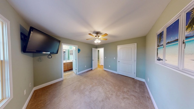 unfurnished bedroom with baseboards, ensuite bathroom, a ceiling fan, and light colored carpet