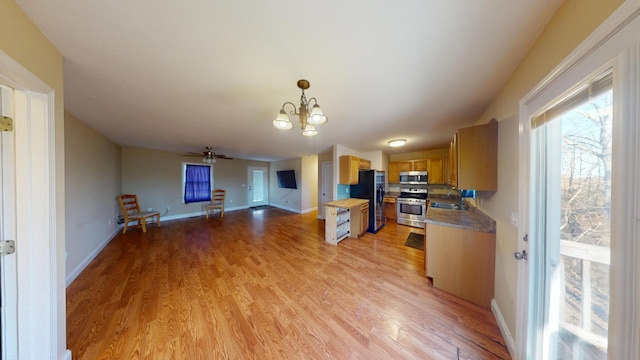 kitchen featuring light wood finished floors, baseboards, appliances with stainless steel finishes, open floor plan, and decorative light fixtures