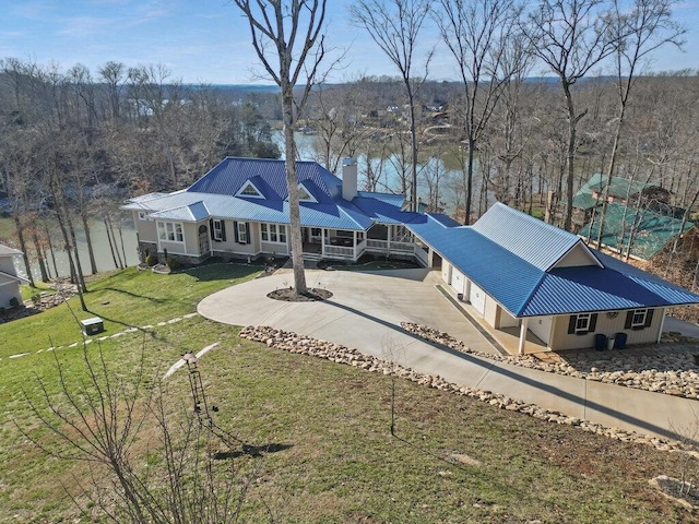 exterior space featuring concrete driveway, a yard, a chimney, and metal roof