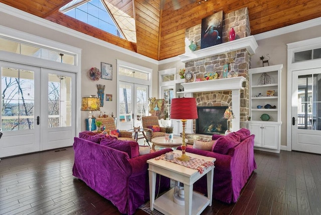 living room with french doors, a high ceiling, ornamental molding, a stone fireplace, and hardwood / wood-style floors