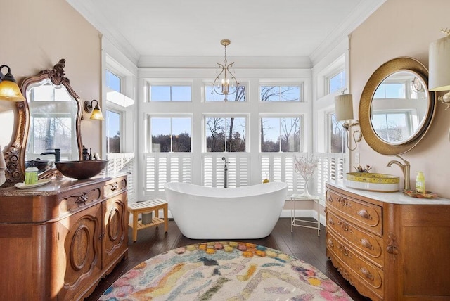 full bath with ornamental molding, wood-type flooring, two vanities, and a freestanding tub