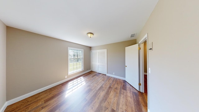 unfurnished bedroom with a closet, wood finished floors, visible vents, and baseboards