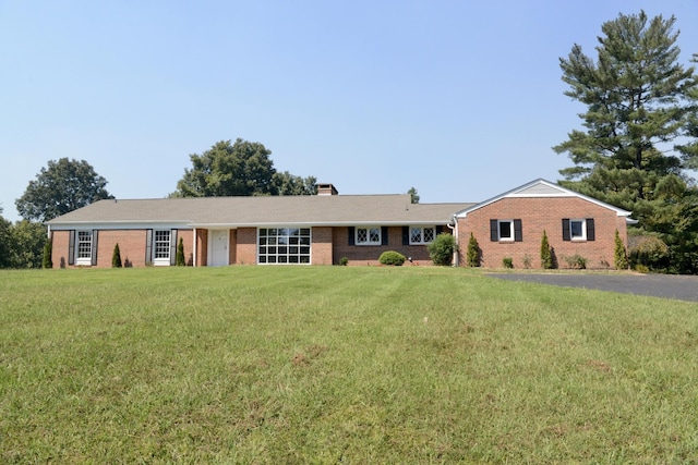 single story home featuring brick siding, a chimney, and a front yard