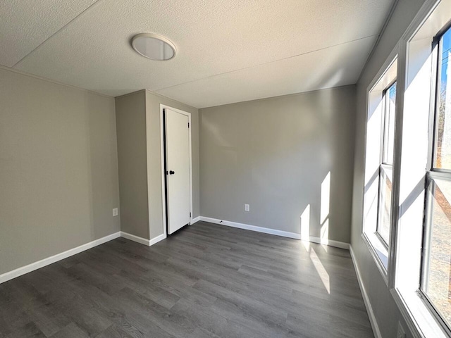 empty room featuring dark wood finished floors, a textured ceiling, and baseboards