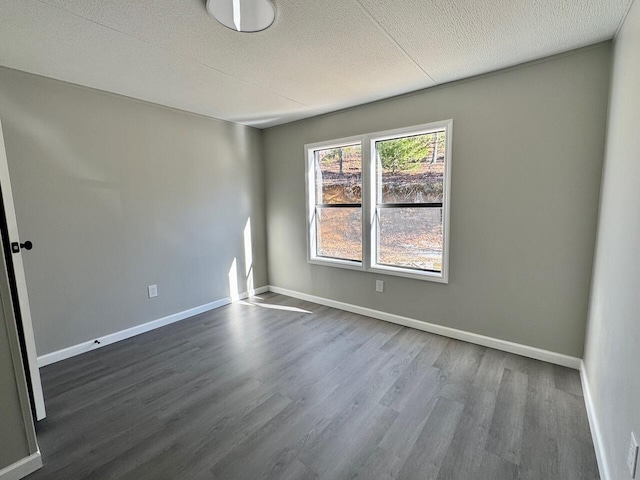 spare room with dark wood-type flooring, a textured ceiling, and baseboards