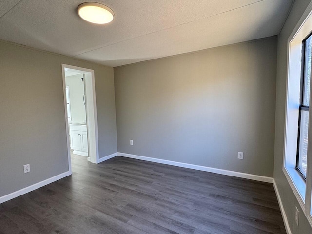 unfurnished room featuring a textured ceiling, dark wood finished floors, and baseboards