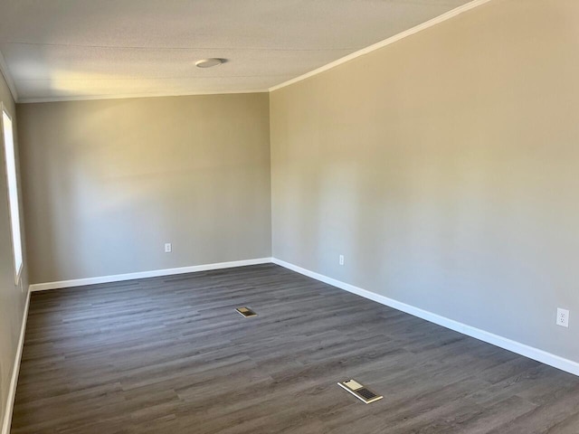 empty room featuring dark wood-type flooring, visible vents, crown molding, and baseboards