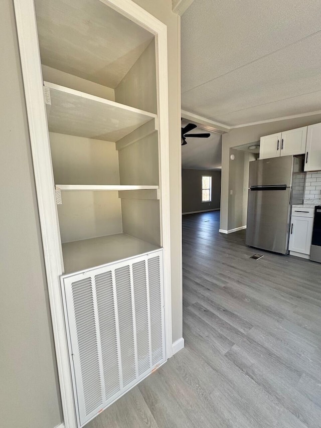 interior space featuring visible vents, a ceiling fan, freestanding refrigerator, white cabinets, and wood finished floors