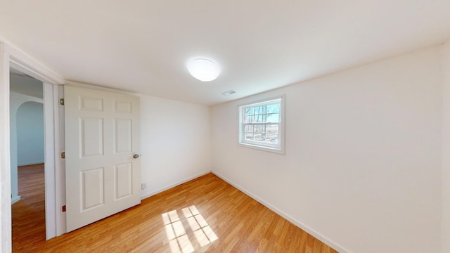 spare room with baseboards, arched walkways, visible vents, and light wood-style floors