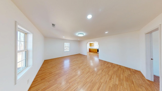 empty room with arched walkways, visible vents, light wood-style flooring, and baseboards