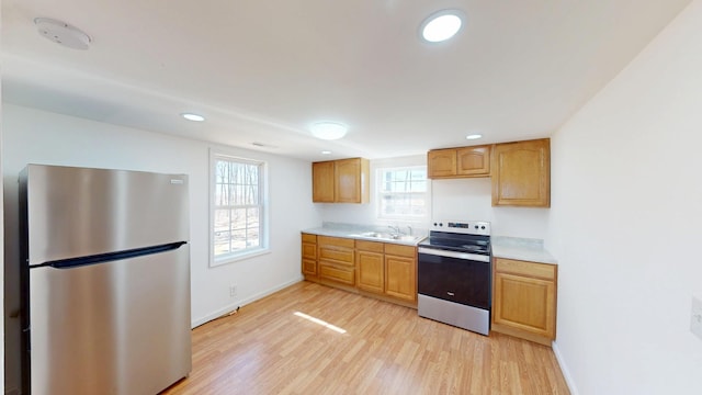 kitchen with stainless steel appliances, light countertops, light wood-style flooring, a sink, and baseboards