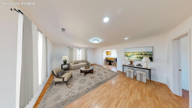 living room with arched walkways, light wood finished floors, recessed lighting, visible vents, and baseboards