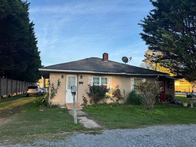 view of front of property with a chimney, a front yard, fence, and stucco siding