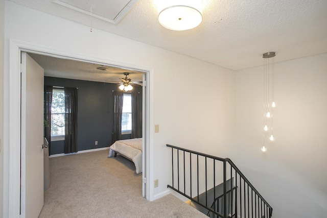 hallway with attic access, light carpet, a textured ceiling, an upstairs landing, and baseboards