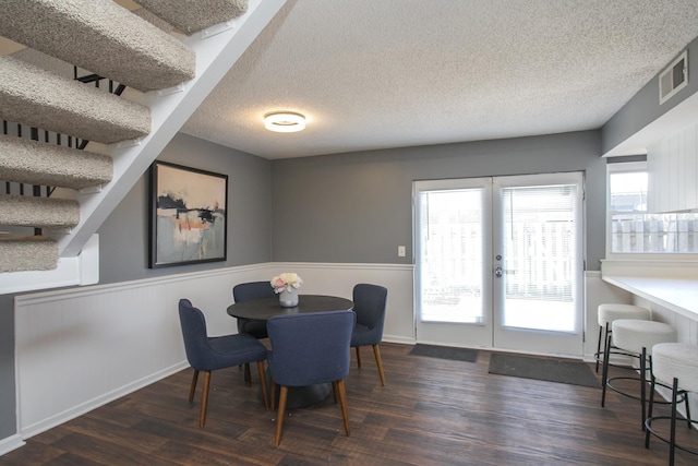 dining area with french doors, visible vents, wainscoting, a textured ceiling, and wood finished floors