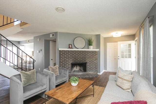 living area featuring visible vents, wood finished floors, stairs, a textured ceiling, and a brick fireplace