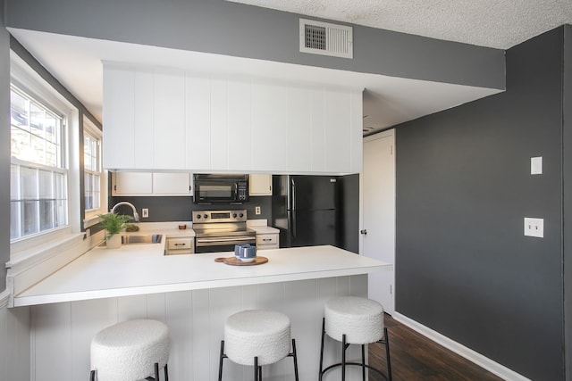 kitchen featuring visible vents, a peninsula, light countertops, black appliances, and a sink