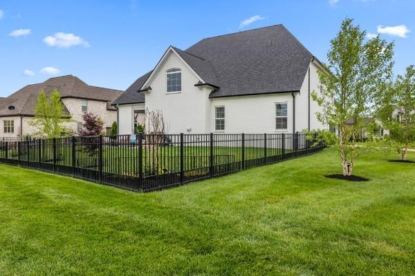 rear view of house with stucco siding, a lawn, and fence