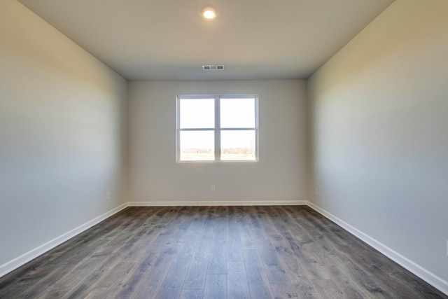 empty room featuring dark wood-style floors, visible vents, and baseboards