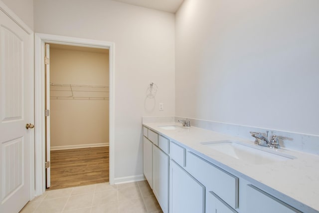 full bath featuring a walk in closet, a sink, baseboards, and tile patterned floors