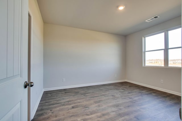 empty room with dark wood finished floors, visible vents, and baseboards