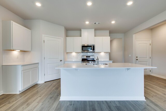 kitchen featuring light countertops, appliances with stainless steel finishes, a kitchen island with sink, a sink, and light wood-type flooring