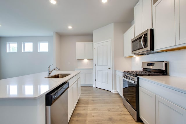 kitchen featuring stainless steel appliances, a sink, light wood-style floors, light countertops, and backsplash