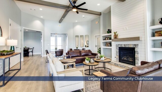 living area with wood finished floors, a high ceiling, a glass covered fireplace, and beam ceiling