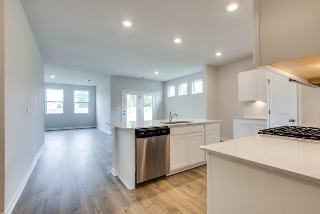 kitchen with light wood finished floors, a center island with sink, baseboards, dishwasher, and a sink