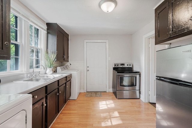 kitchen featuring stainless steel appliances, light wood-style flooring, washing machine and dryer, a sink, and dark brown cabinets