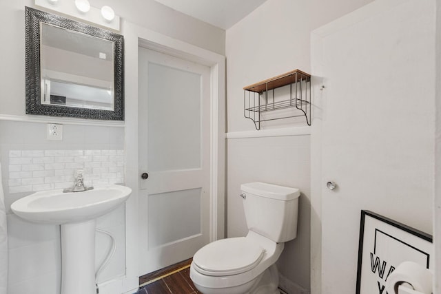 half bathroom featuring wainscoting, tile walls, toilet, and wood finished floors