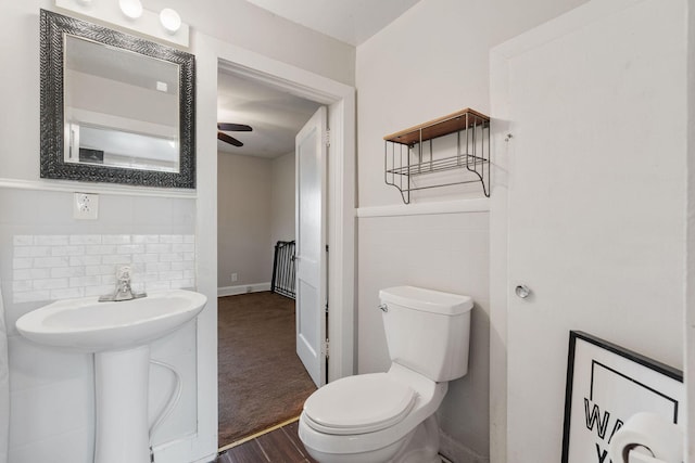 bathroom featuring toilet, wood finished floors, tile walls, a ceiling fan, and wainscoting