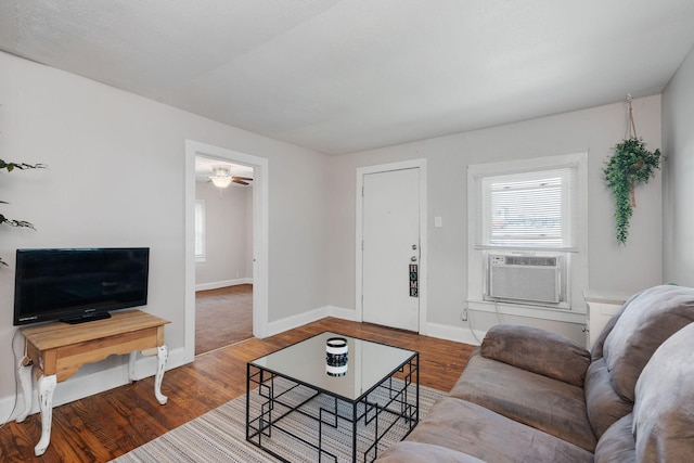 living room with cooling unit, baseboards, and wood finished floors