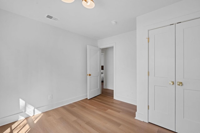 unfurnished bedroom with a closet, visible vents, light wood-style flooring, and baseboards