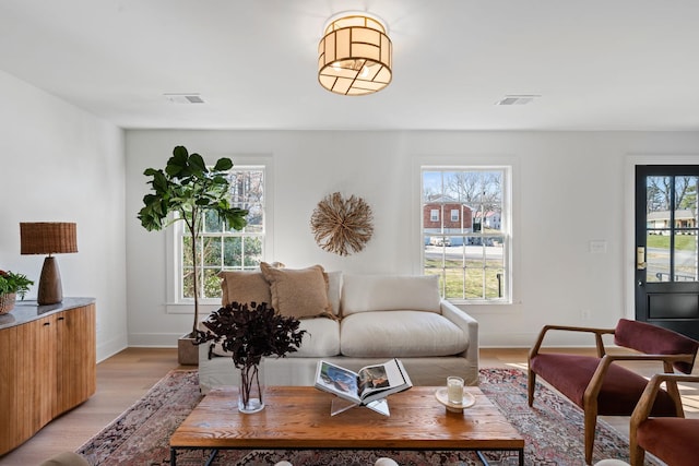 living area with baseboards, light wood-type flooring, visible vents, and a healthy amount of sunlight