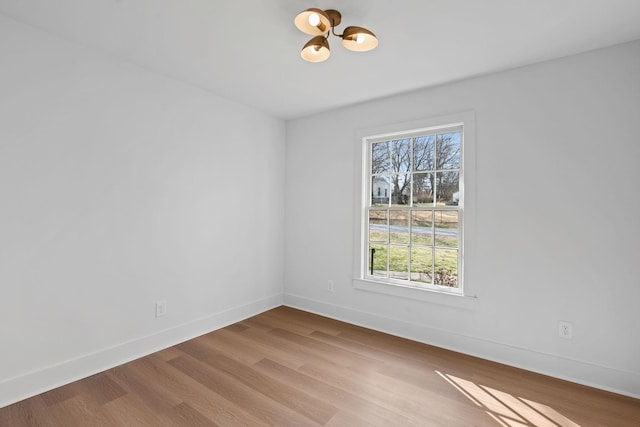 unfurnished room featuring an inviting chandelier, baseboards, and wood finished floors