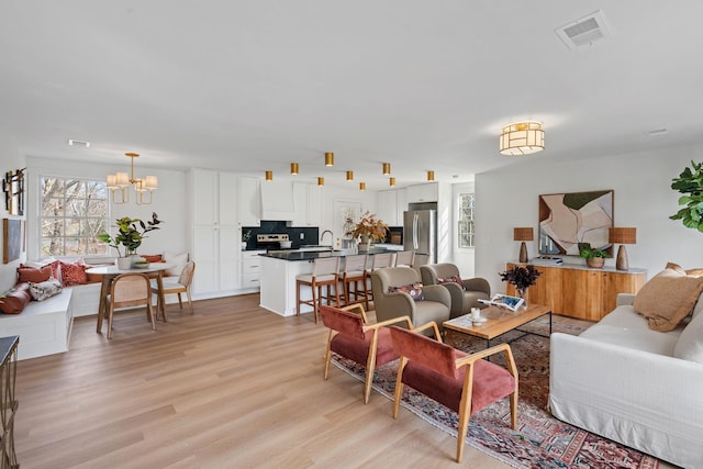 living area featuring light wood-style flooring, visible vents, and a chandelier