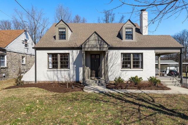 view of front of property with brick siding, a shingled roof, concrete driveway, a chimney, and a front yard