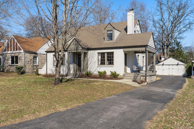 view of front facade with brick siding, a detached garage, a chimney, an outdoor structure, and a front lawn