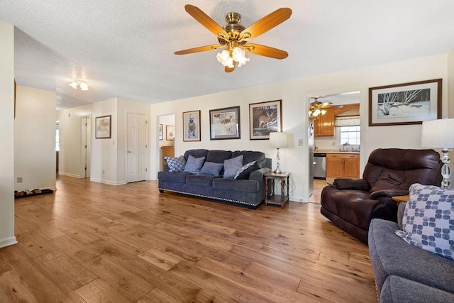 living area with light wood-type flooring, ceiling fan, baseboards, and a textured ceiling