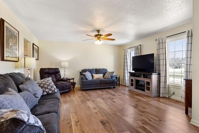 living area featuring wood-type flooring, ceiling fan, a textured ceiling, and baseboards