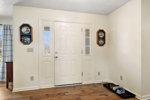 foyer entrance with a textured ceiling, baseboards, and wood finished floors