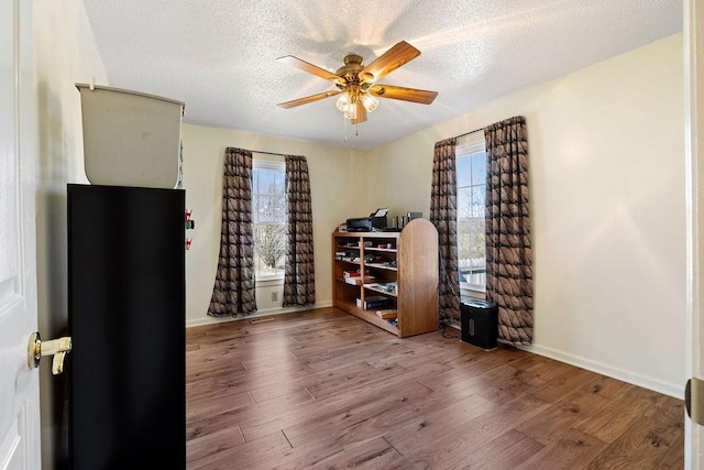 interior space featuring ceiling fan, a textured ceiling, baseboards, and wood finished floors