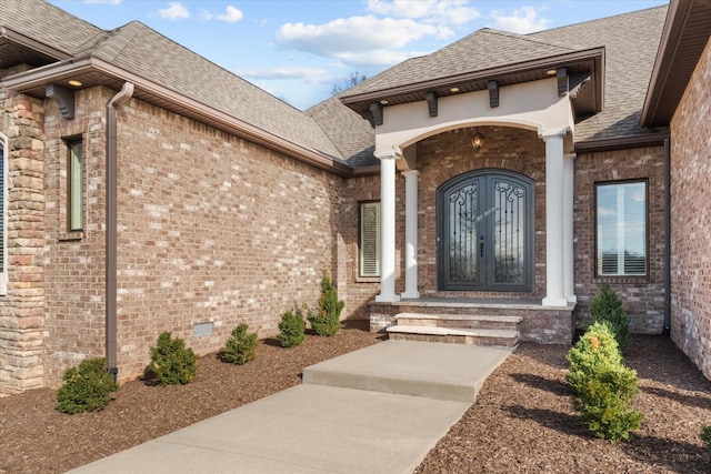 property entrance featuring crawl space, roof with shingles, french doors, and brick siding