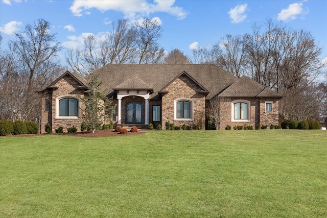 french country inspired facade with stone siding, a front lawn, and roof with shingles