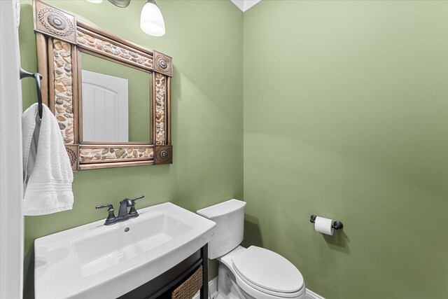 half bathroom with vanity, toilet, and baseboards