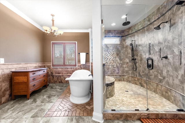 bathroom with an inviting chandelier, a shower stall, a freestanding bath, and wainscoting