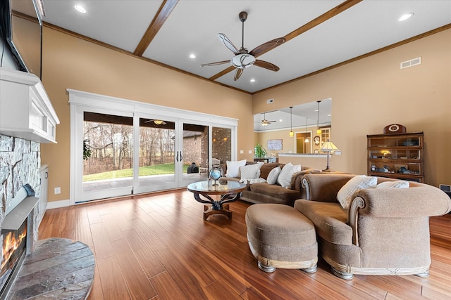 living area featuring visible vents, a ceiling fan, ornamental molding, light wood-style floors, and a fireplace