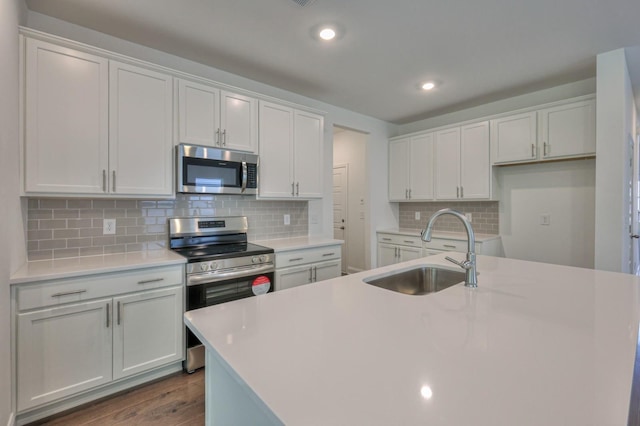 kitchen with dark wood-style flooring, a sink, light countertops, appliances with stainless steel finishes, and a center island with sink